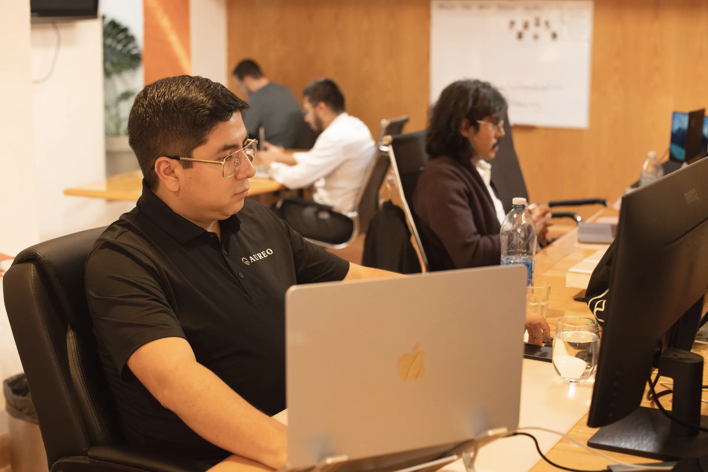 Gustavo Flores Echaiz working at the Aureo office, with the team in the background